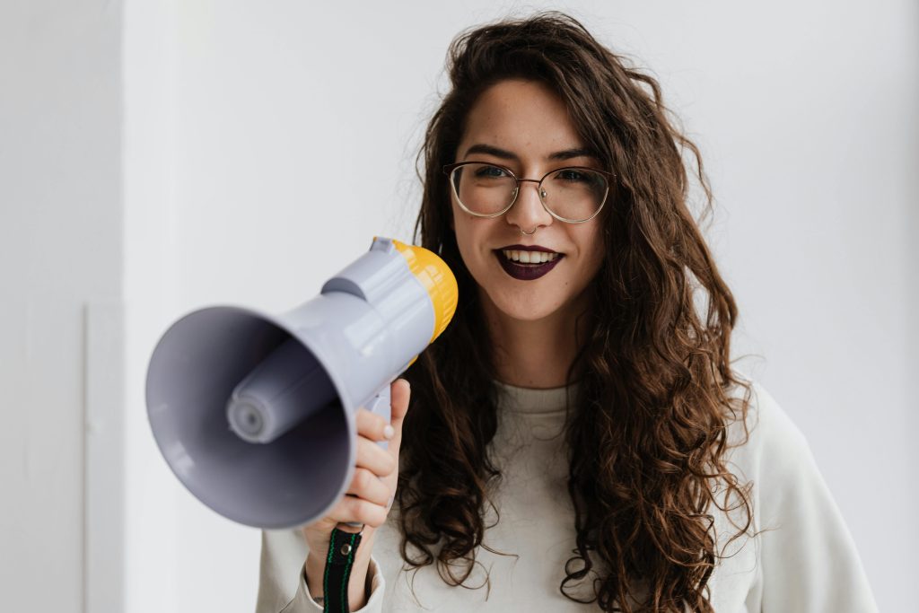 Cheerful woman with glasses and a megaphone against a white background.